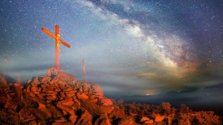 Image of 3 crosses on a hill with a galaxy of stars in the background.