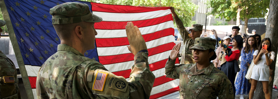 Image of an ROTC cadet getting sworn in outside with an American flag in the background. 