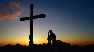Man Praying by a Cross at Sunset