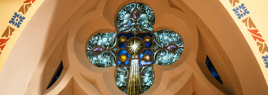An image of a stained glass window in the shape of a cross. 