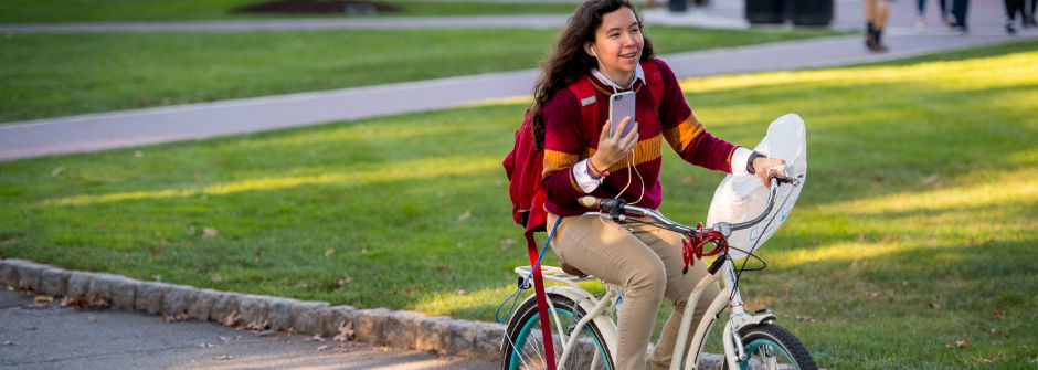 Student on the go with her phone on a bike.