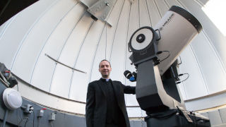 Photo of Father Laracy in front of a telescope