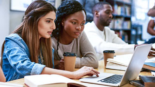 Two students looking at a laptop screen in the library.