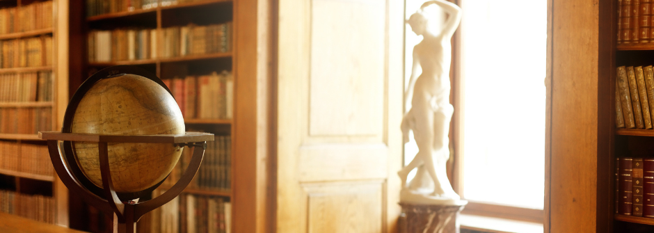 Image of a globe and a marble statue of a woman by a window in a library. 