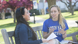 Two students sitting talking on a bench on campus.