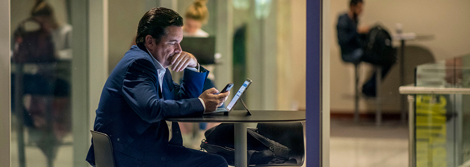 Going Virtual Header - a man using his phone while sitting in front of his laptop