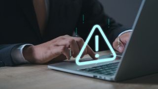 Person using a laptop with a digital security warning icon displayed on the screen.