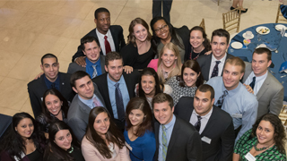 Image of a student wearing a school of business shirt with a backpack standing on campus outside and smiling. Associate Professor Kurt Rotthoff, Ph.D.Buccino students at a dinner. 