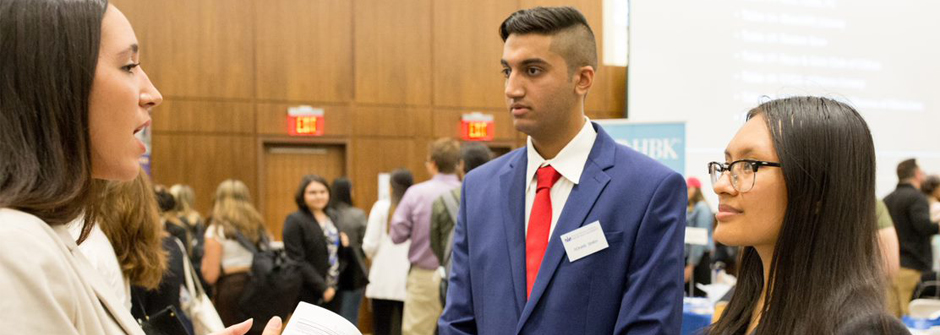 Image of two students dressed up for the career fair and speaking to a potential employer. 