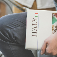 Image of a male sitting holding an Italy textbook in a street. 
