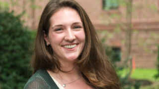 Kiersten Lynch wearing a green sweater and standing in front of a brick building