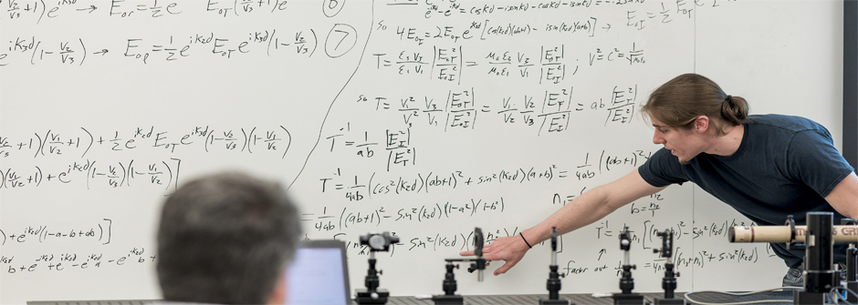 People at a white board working on physics equations.