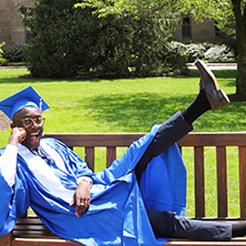 Martin Tettey sitting on a bench while wearing graduation attire. x222