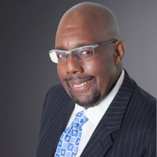 Headshot of Matthew Horace in a suit on a grey background. 