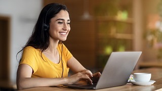 Student with headphones on smiling while sitting at their computer.