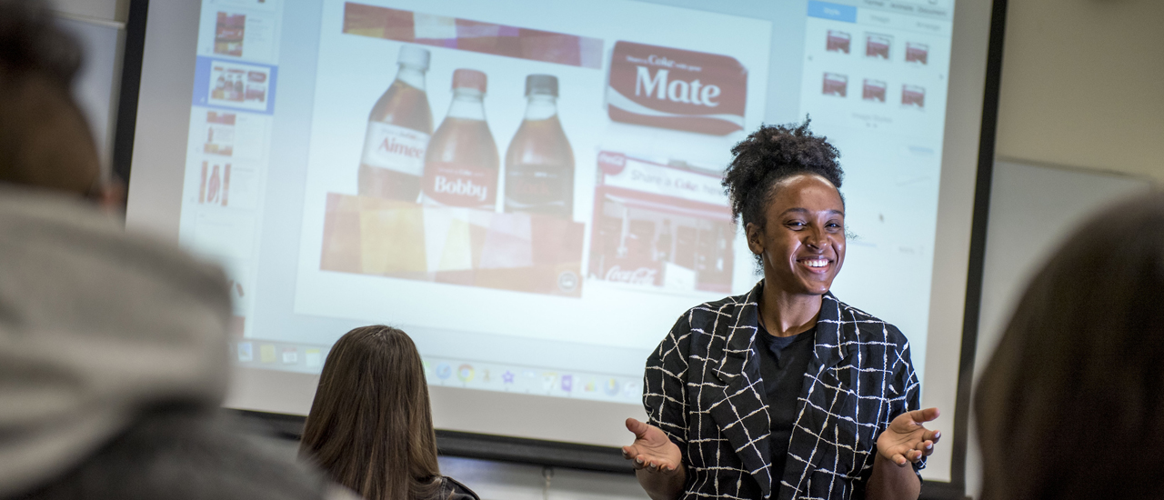 Image of a woman doing a presentation with slides in the background related to the branding of Coca Cola. 