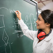 A female engineering student working on a chalk board figuring out a physics equation.