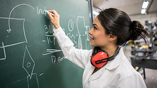 A female engineering student working on a chalk board figuring out a physics equation.