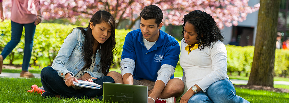 Three students looking at a laptop outside.