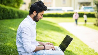 Man sitting on computer on the grass.