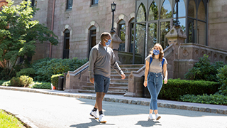 Two students wearing masks walking on campus in front of Presidents Hall.