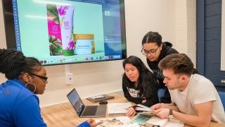 Students working on a class project in front of a tv monitor and laptop.