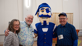 Three alumni members posing with the Seton Hall pirate mascot. 