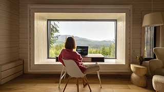 A photo of a person sitting in front of a window working on a computer.