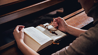Individual reading the Bible and holding Rosary beads.