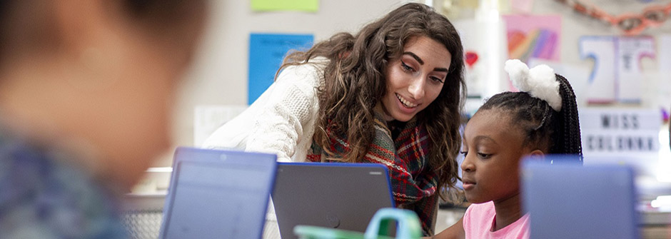 Teacher guiding young student working on laptop.