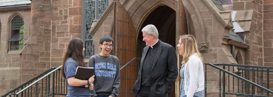 Campus community A priest laughing with students outside the Chapel of Immaculate Conception.