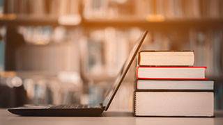 An open laptop next to a stack of textbooks.