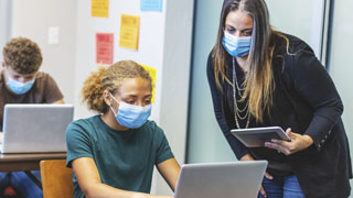 Student and teacher interacting in class while wearing face masks.