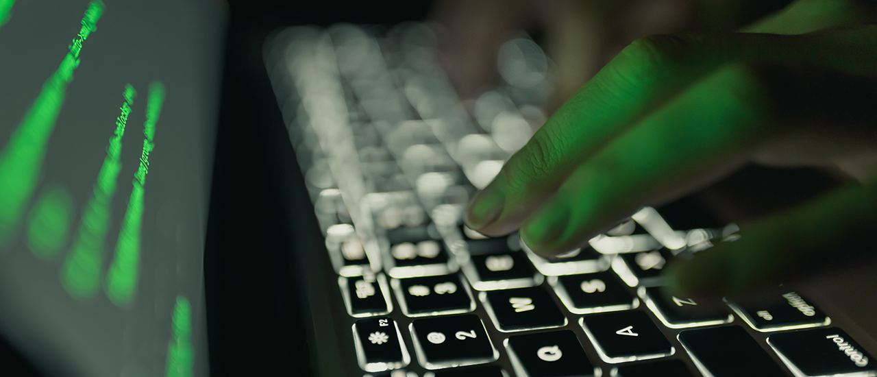 A hand pressing the keys on a lit up keyboard at night 