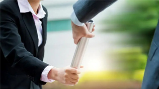 Two employees in a race dressed professionally passing the baton to each other.