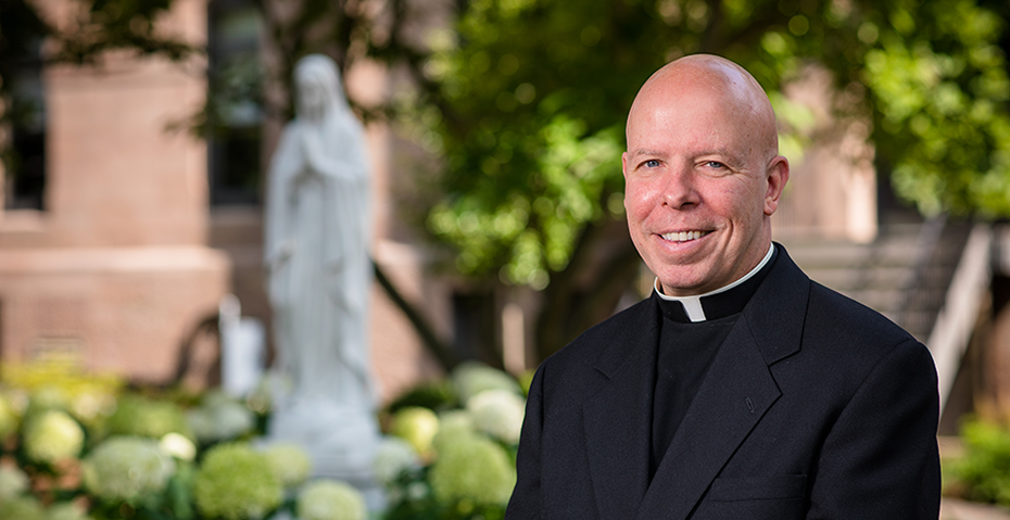 Father Colin Kay at Seton Hall in front of Blessed Mother statue