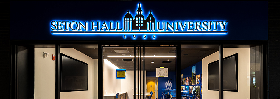 View of the front of the Seton Hall Gateway Center space looking in with lighted sign of the Seton Hall University logo above the doors.