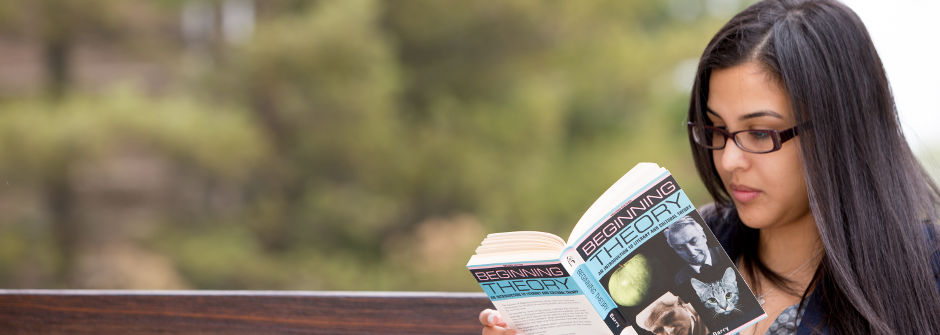 Student reading a book on a bench. 