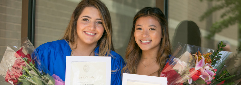 Two Honors students holding bouquets and their honor citation awards. 