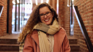 Portrait photo of Emily High smiling and standing in front of stairway.