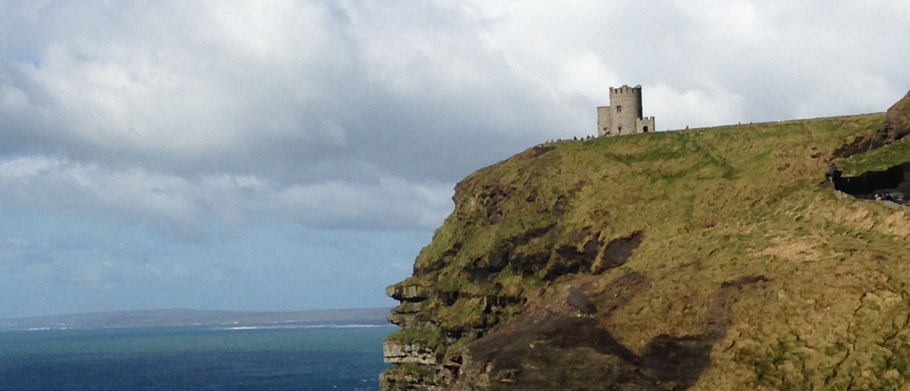 Irish coast with a castle on a cliff overlooking the water. 