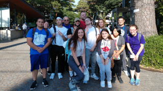 Four people are waiting to cross the street in Tokyo, Japan. The four people are facing away from the camera, backs in the photo.Students who participated in the Study Abroad program in Tokyo, Japan. The students are holding up a Seton Hall flag in the photo.Four people are waiting to cross the street in Tokyo, Japan. The four people are facing away from the camera, backs in the photo.