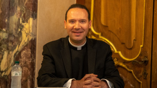 Father Laracy sitting with hands folded at table. 