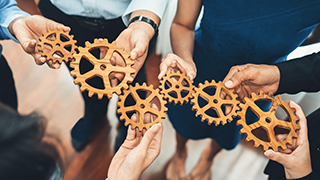 People holding gears working to fit them together.