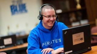Seton hall student on their laptop. Wearing headphones and a blue Pirates sweatshirt.