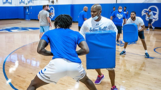 Shaheen Holloway practicing with Kadary Richmond of the Pirates basketball team in the gym while holding a pad.