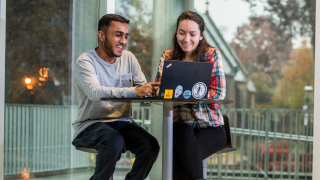 A male and female student looking at a computer.