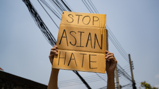 A person holding a Stop Asian Hate cardboard cut out sign.