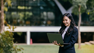 student smiling and holding an open laptop outside