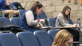 Student signing paperGirl writing on a paperTwo students in a lecture hall